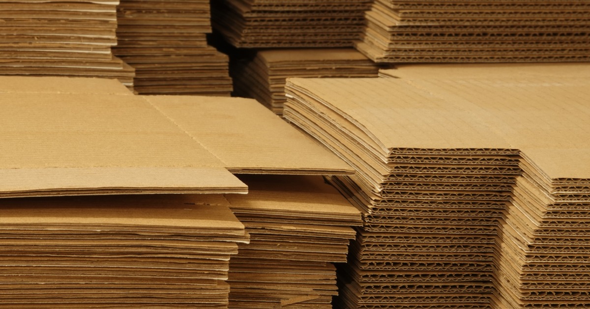 Several stacks of flat corrugated boxes. The stacks have both single- and double-wall corrugated boxes.