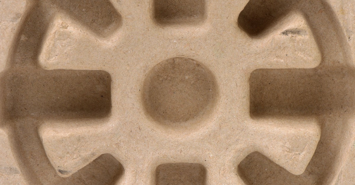 A close-up of the inside of a molded pulp packaging insert. The insert is shaped like a cogwheel.