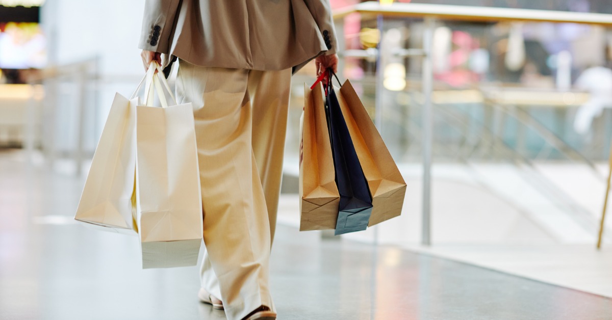 A close-up of someone walking away in a mall while holding several luxury shopping bags in both hands.