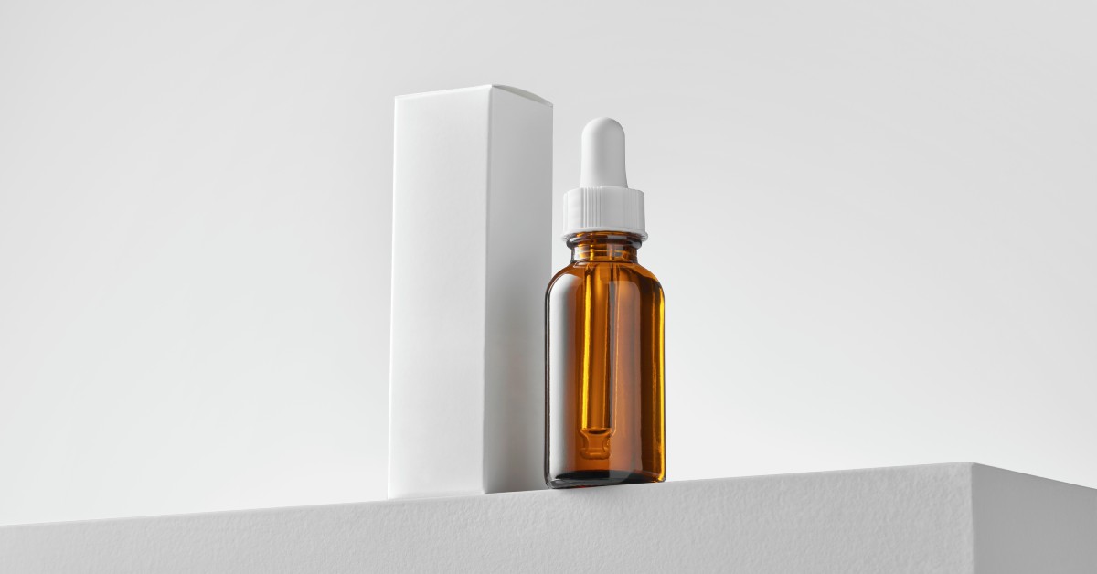 A serum bottle with a blank label that rests next to a white cosmetic box that is not labelled.