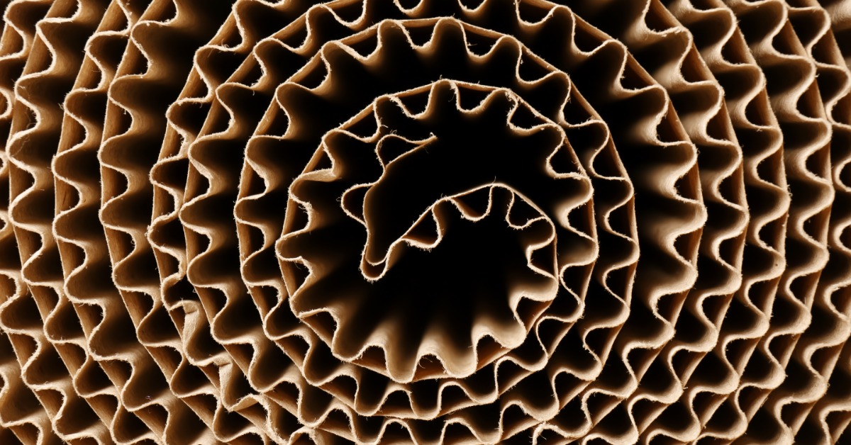 A close-up of corrugated cardboard material rolled up in a tight spiral. The wavy texture of the corrugation is visible.
