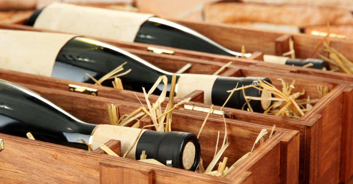 A close-up of multiple wine bottles lying on the side inside individual wooden boxes filled with dry hay.