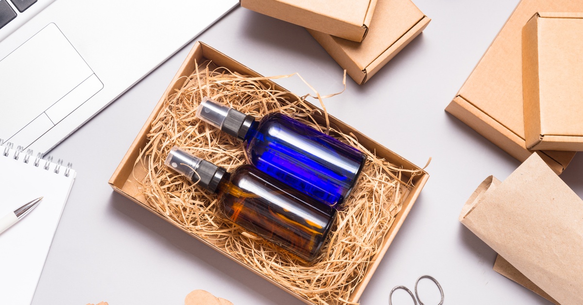 An aerial view of a cardboard box filled with thin cardboard cutouts and two small glass spray bottles on a desk.