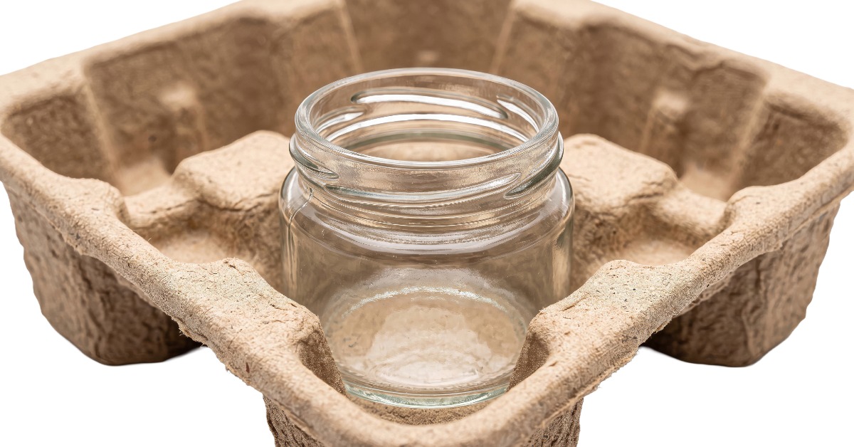 A close-up of a glass mason jar without a top placed on a compartment of a molded pulp tray with four divisions.